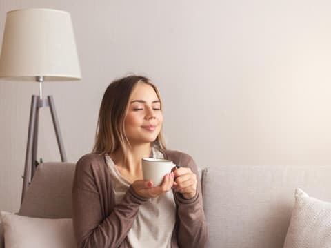 Frau sitzt auf dem Sofa und hält einen Kaffee in der Hand