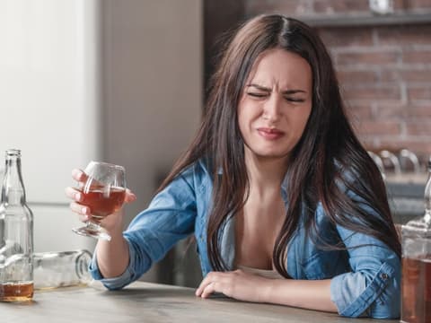Frau verzieht das Gesicht und hält ein Glas in der Hand