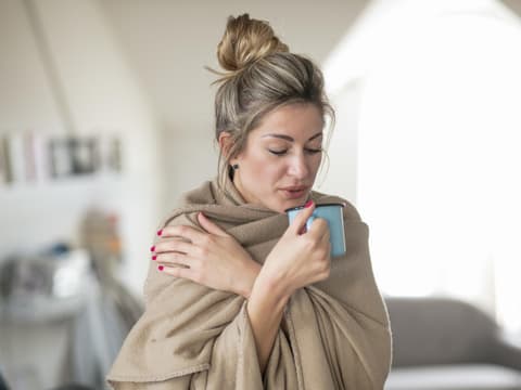 Eine Frau ist in eine Decke eingewickelt und trinkt Tee