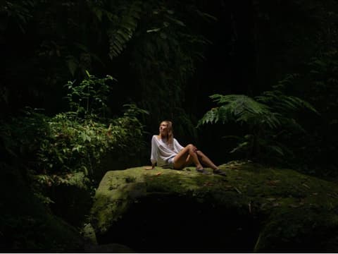 Eine Frau sitzt auf einem Felsen im Regenwald