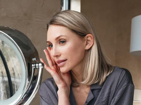Eine Frau sitzt vor einem Kosmetikspiegel