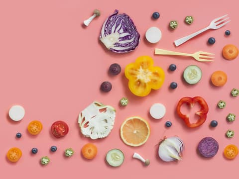 Gemüse wie Paprika, Kohl, Blumenkohl, Paprika und mehr halbiert und dekorativ auf rosafarbenem Hintergrund drapiert