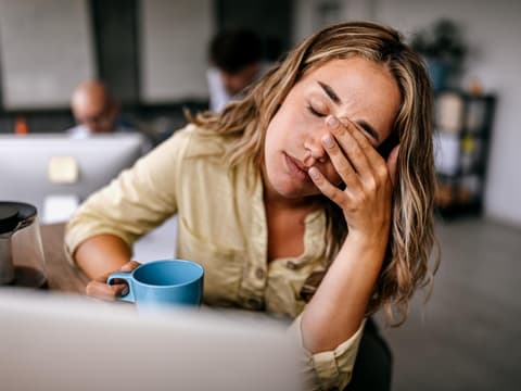 Eine Frau hält müde ihre Kaffeetasse fest