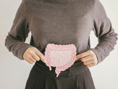 Eine Frau hält eine Abbildung des Darmtraktes aus Papier an die Stelle, wo der Darm auch liegt.