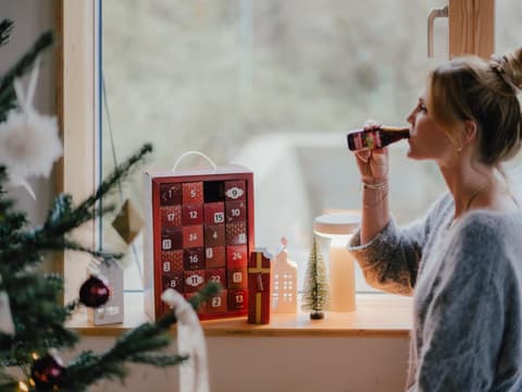 Eine junge Frau hat das erste Türchen ihres Rabenhorst-Adventskalenders geöffnet und trinkt einen Schluck aus der Mini-Saftflasche 