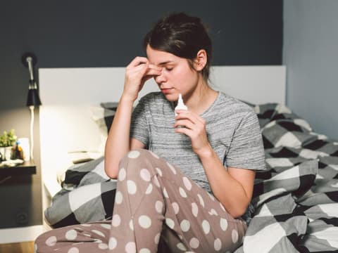 Frau mit Nasenspray im Bett