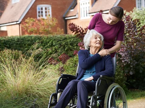 Seniorin im Rollstuhl mit Frau, draußen