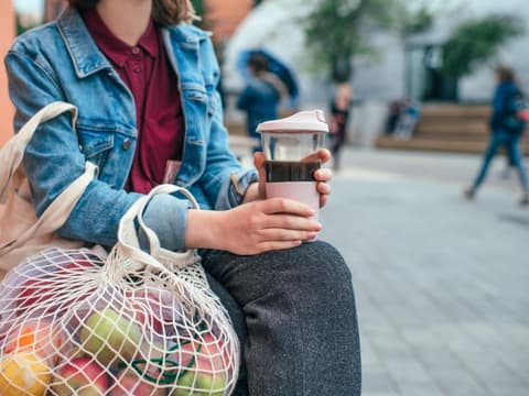 Frau mit nachhaltigen Alternativen mit Obstnetz und Kaffeebecher