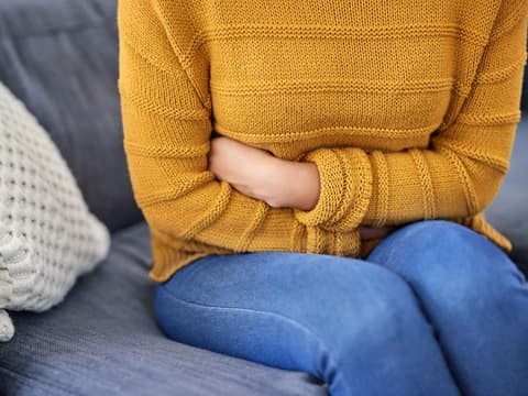 Frau sitzt auf Sofa und hält sich den Bauch