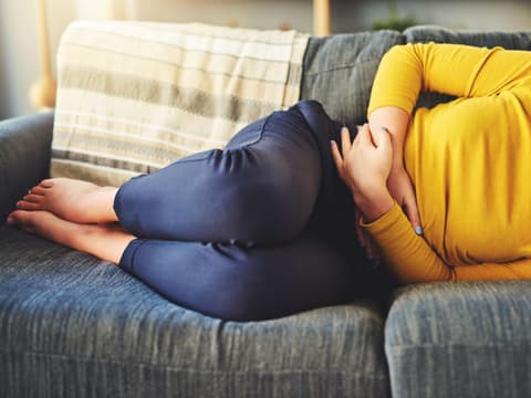 Frau mit Unterleibschmerzen auf dem Sofa