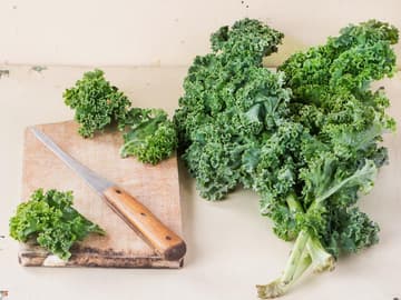 Grünkohl liefert für ein Gemüse enorm viel Protein: 4,3 Gramm pro 100 Gramm. Grünkohl auf einem Schneidebrett