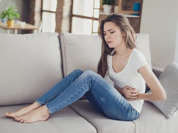 Frau sitzt mit Bauchschmerzen auf dem Sofa Frau sitzt mit Bauchschmerzen auf dem Sofa