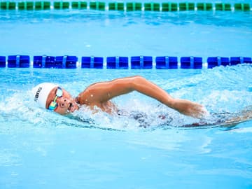 Frau mit Schwimmbrille und Schwimmkappe krault durchs Wasser Frau mit Schwimmbrille und Schwimmkappe krault durchs Wasser