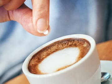 Hand mit Süßstofftablette über einer Tasse Kaffee Hand mit Süßstofftablette über einer Tasse Kaffee