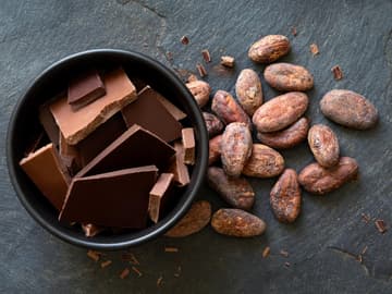 Schokoladenstückchen in einer Keramikschale neben Kakaobohnen Schokoladenstückchen in einer Keramikschale neben Kakaobohnen