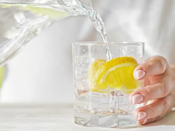 Wasser wird in ein Glas mit Zitrone gegossen Wasser wird in ein Glas mit Zitrone gegossen