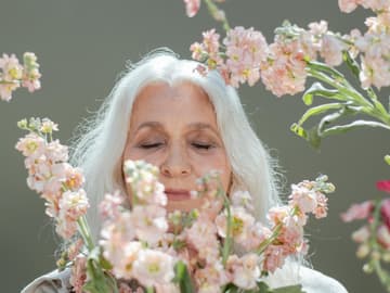 Frau mit grauen Haaren riecht an Blumen Frau mit grauen Haaren riecht an Blumen