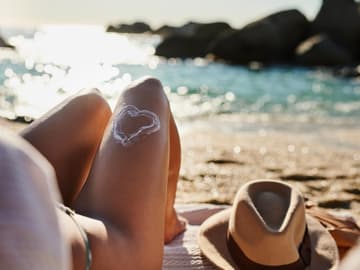 Mineralische Sonnencreme ohen chemische Filter Frau liegt an Strand mit Hut neben ihr