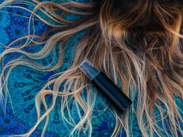 Hitzeschutzspray mit Nachhaltigkeitsfaktor Frau posier tmit langen Haaren auf Batikteppich