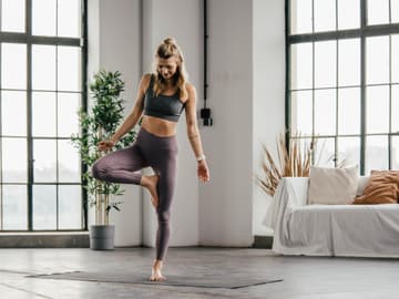 Balanceübungen setzen Fitness voraus Frau steht auf einem Bein in Wohnzimmer