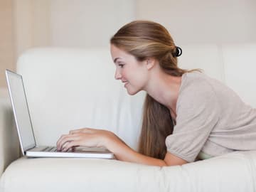 Frau liegt mit Laptop auf einer weißen Couch Frau mit Laptop