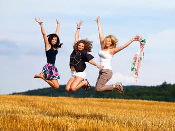 Frauen lachen auf einem Feld und springen in die Luft Frauen lachen auf einem Feld