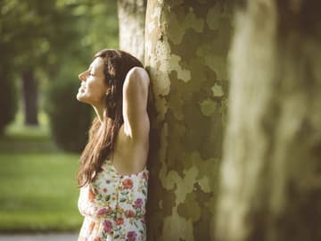 Frau steht lachend am Baum in einem Kleid Frau am Baum