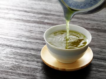 Grüner Tee hilft durch seine Antioxidantien, das Krebsrisiko zu reduzieren Grüner Tee wird in eine Tasse gegossen