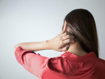 Frau-kratzt-sich Frau juckt sich mit der Hand am Nacken.