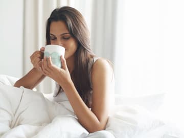 Frau-liegt-flach-PeopleImages-iStock Frau trinkt Tee und gönnt ihrem Körper Erholung.