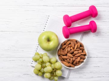 Mit Sport und Ernährung gesund zunehmen Apfel, Weintrauben, Mandeln und Kurzhanteln liegen auf einem Block