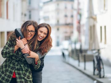 Zwei_Frauen_lachen Zwei lachende Frauen auf der Straße umarmen sich