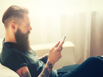 Mann_mit_Vollbart Mann mit Vollbart auf Couch mit Handy