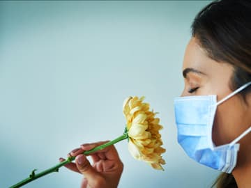 Mundschutz_Allergie_Heuschnupfen Frau mit Mundschutz riecht an Blume